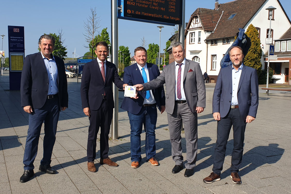 Vertreter RVR und Bürgermeister vor dem Bahnhof mit Klimaplakette in der Hand