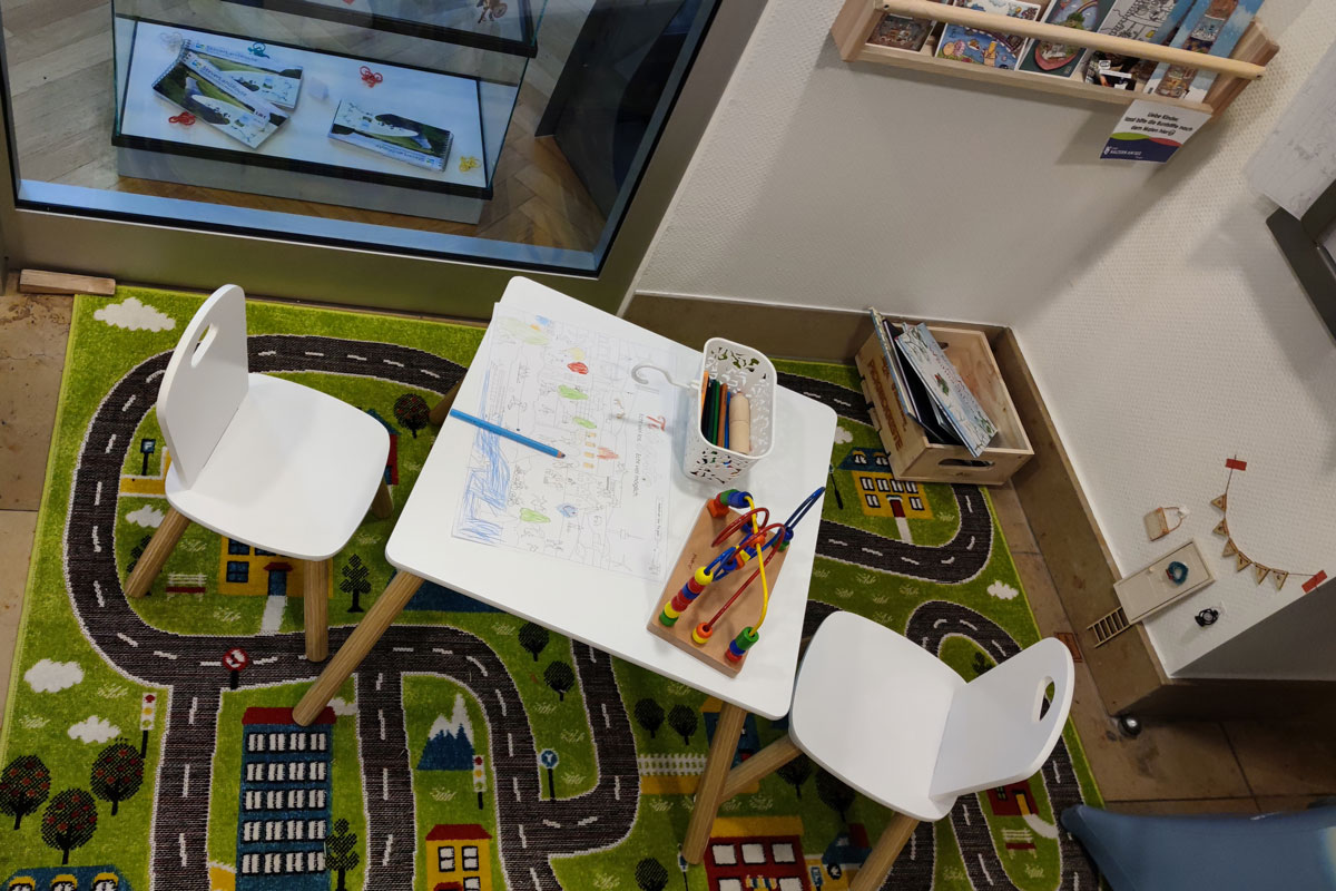 Ein weißer Tisch mit zwei Stühlen, auf dem ein Ausmalbild zu sehen ist. Der Tisch steht auf einem Spieleteppich