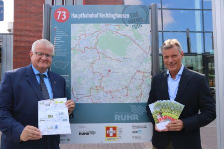 Vor der Infotafel zum radrevier.ruhr am Hauptbahnhof präsentieren Bürgermeister Christoph Tesche und Stadtkämmerer Ekkehard Grunwald den neuen Infoflyer, der alle Details zum Rundkurs bietet, der die Römer-Lippe-Route mit dem RuhrtalRadweg miteinander verbindet. Foto -  Stadt RE
