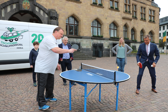 Bürgermeister Christoph Tesche (r.) probiert ein Angebot des Ferientreffs direkt selbst aus: Alexander Murek vom Deutschen Tischtennis Bund (vorne l.) präsentiert das Tischtennis-Schnuppermobil auf dem Rathausplatz. Jugendamtsleiter Volker Hülsmann (3.v.l.) und Ferientreffkoordinatorin Tanja Alshut (2.v.r.) präsentierten zuvor Auszüge des diesjährigen Ferientreffprogramms. 