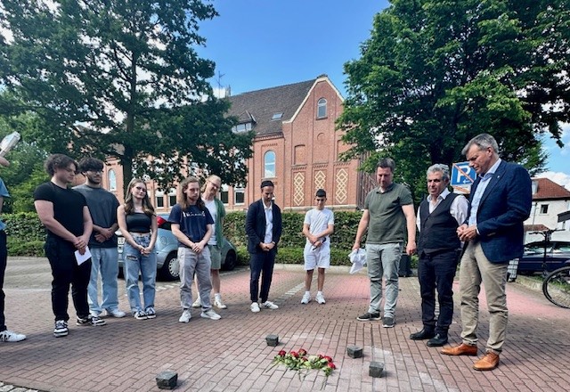 Gemeinsam mit Schülerinnen und Schülern, Lehrern und Isaac Tourgman, Kantor der Jüdischen Kultusgemeinde, enthüllten Bürgermeister Christoph Tesche die sieben neu verlegten Stolpersteine, die an der Friedhofstraße an die Familie Jäckel erinnern. Foto: Stadt RE