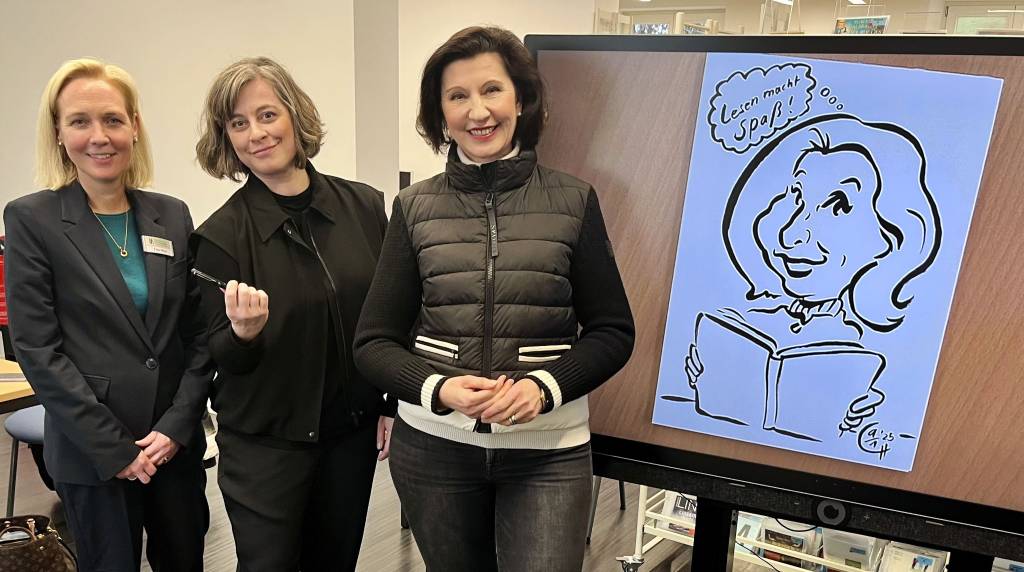 Über das neue Smartboard in der Zweigstelle der Stadtbibliothek in Recklinghausen-Süd freut sich die Bibliotheksleiterin Sandra Hilse (l.). Charlotte Hofmann, Medienpädagogin und Comiczeichnerin, fertigte gleich einmal eine Zeichnung der stellvertretenden Bürgermeisterin Marita Bergmaier (r.) an. Foto: Stadt RE 