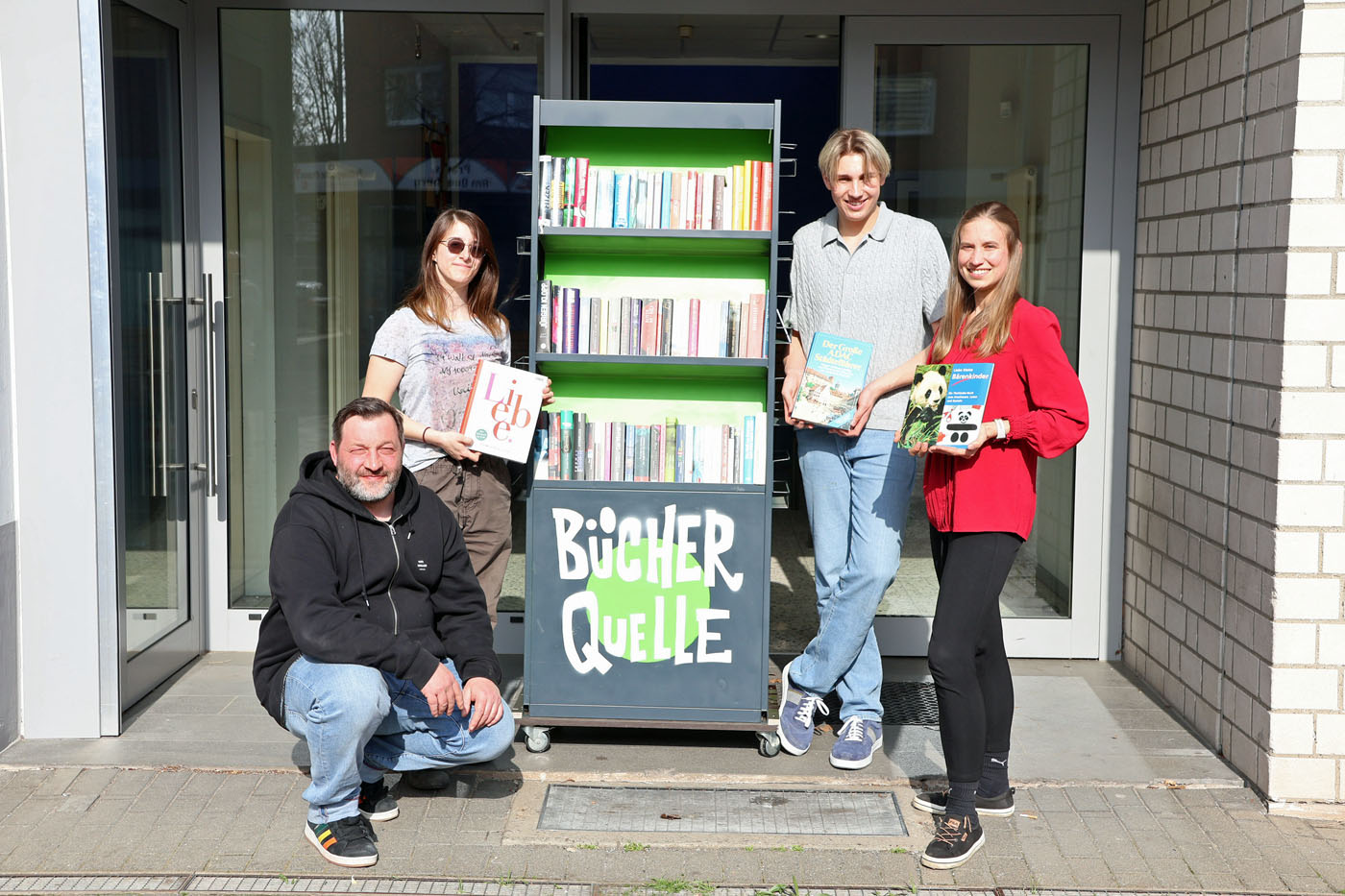 Frederik, Guilia sowie Markus Becker (Leiter der Gestaltungswerkstatt) und Marie Quakulinski (Einrichtungsleitung) haben die &bdquo;B&uuml;cherquelle&ldquo; mit aufgebaut. 