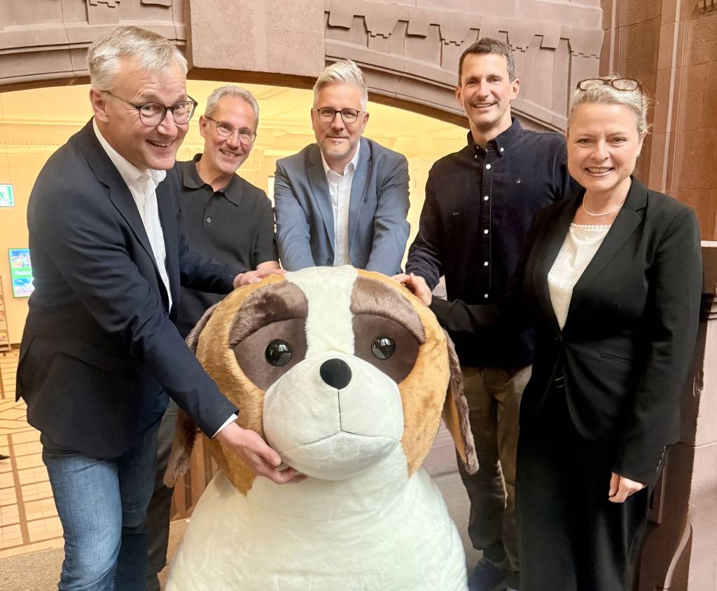 B&uuml;rgermeister Axel Tschersich (l.) pr&auml;sentierte zusammen mit &bdquo;Benni&ldquo; und den Arena-Gesch&auml;ftsf&uuml;hrern Lars Tottmann (2.v.l.) und Marius Ebel (2.v.r.) sowie der Ersten Beigeordneten Silke Ehrbar-Wulfen und Hendrik E&szlig;ers, Leiter des Fachbereichs Wirtschaftsf&ouml;rderung, Standortmanagement und Stadtmarketing, erste Details zur Rathausshow bei &bdquo;Recklinghausen leuchtet 2026&ldquo;. Foto: Stadt RE